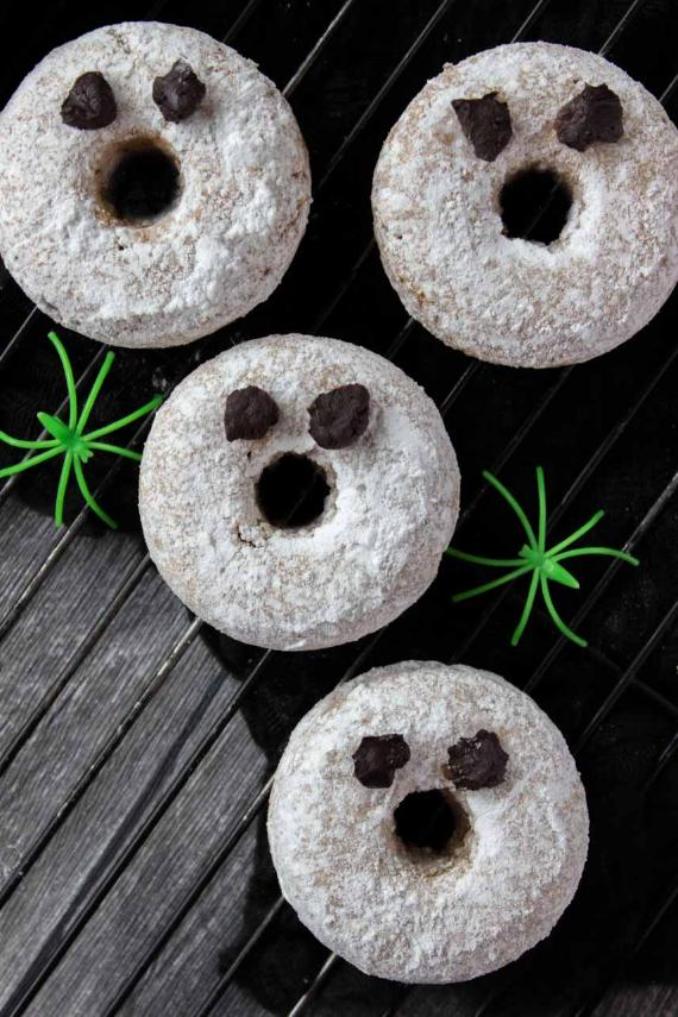Four decorated doughnuts with cartoon eyes and small plastic spiders, arranged on a white plate.