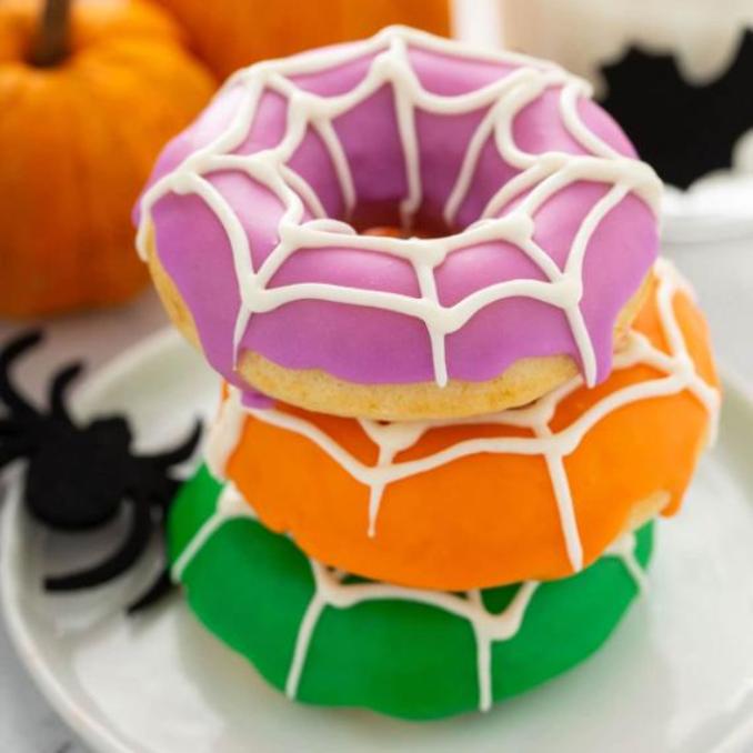 A white plate holds three donuts adorned with spider web decorations.