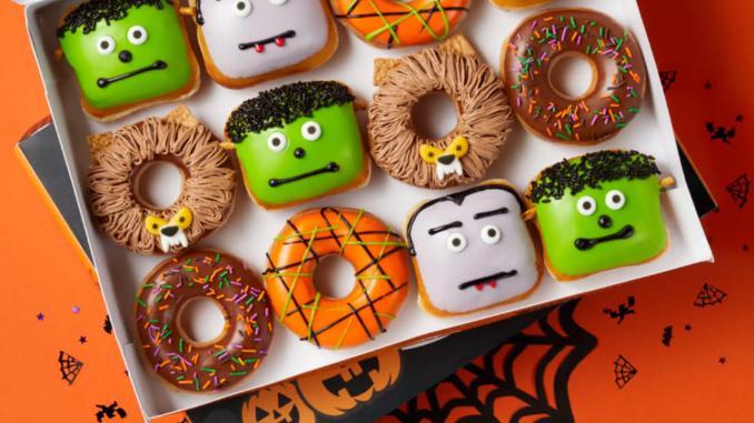 A colorful assortment of Halloween donuts in a box, featuring various whimsical faces and spooky decorations.