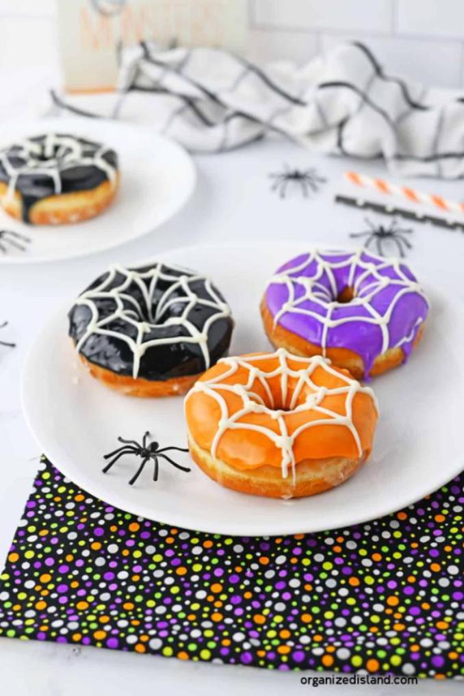 A plate featuring three donuts decorated with intricate spider webs, perfect for a Halloween celebration.