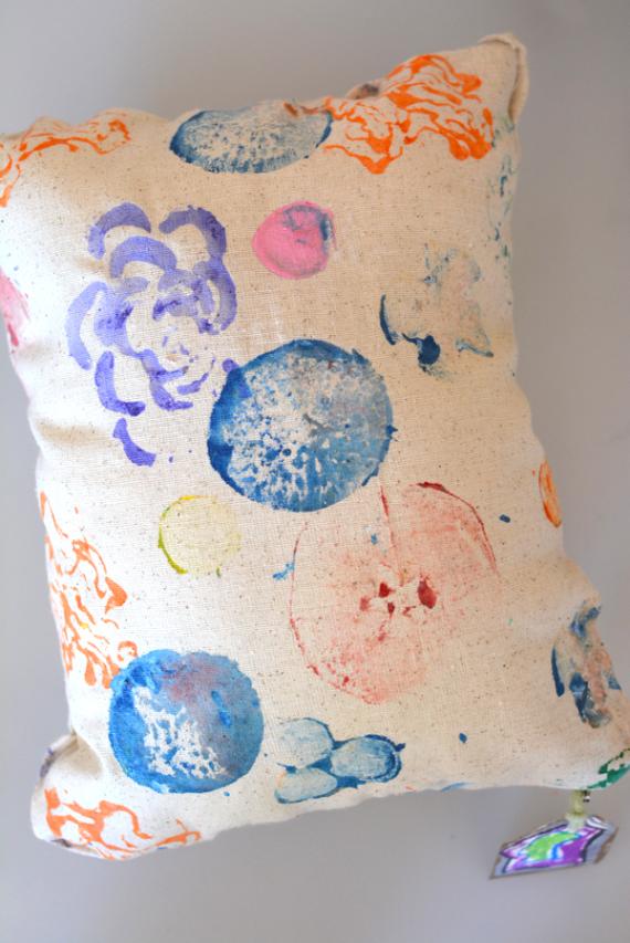 Beige pillow with abstract, colorful paintbrush patterns in blue, pink, orange, and yellow, creating an artistic and playful feel.