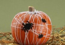 Great No Carve Halloween Pumpkin Decorating Ideas: So simple to prepare! An orange pumpkin wrapped in white yarn to look like a cobweb with small black toy spiders on a bed of straw.