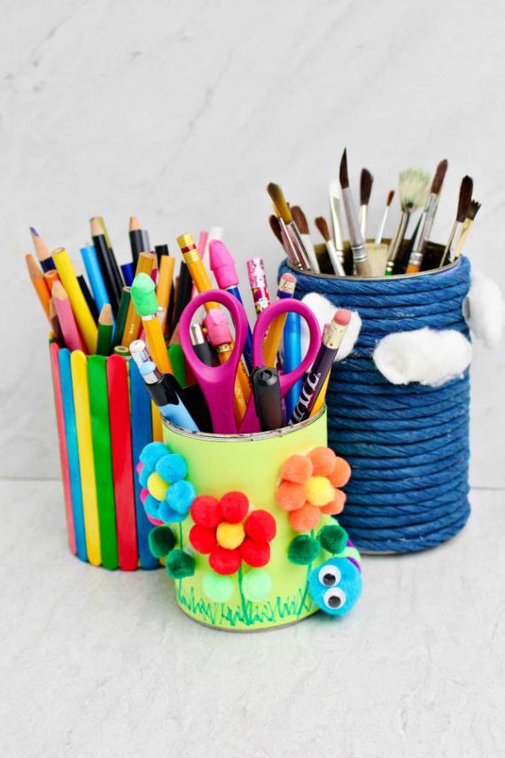 Colorful desk organizers made of decorated pencil holders. One has rainbow sticks, another floral pom-poms, creating a creative, cheerful vibe.
