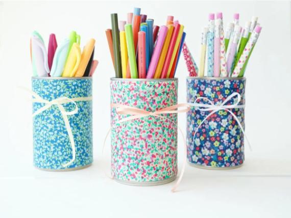 Three tin cans wrapped in floral fabric hold pens, markers, and pencils. Each can is tied with a ribbon, creating a colorful, cheerful arrangement.