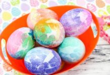 Easter Egg Decorating Ideas – Easter Egg Crafts A vibrant orange bowl holds six colorful tie-dye Easter eggs/ tissue Paper Mosaic Eggs in pastel shades of blue, pink, green, and purple. The background features a colorful, patterned design.