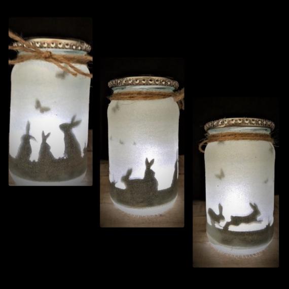 Three Easter Mason Jar Lantern with soft white light, each featuring silhouettes of rabbits and butterflies. Jars are decorated with twine, creating a whimsical, cozy mood.