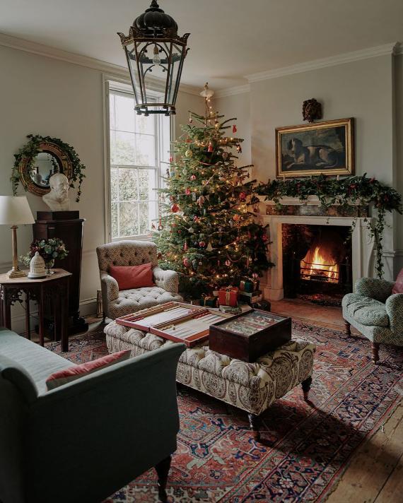 Cozy rustic Christmas living room featuring decorated pine tree near crackling stone fireplace with farmhouse holiday decor and ambient candlelight