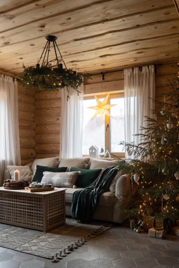 Cozy rustic Christmas log cabin living room with neutral sofa, evergreen plaid throw, decorated tree, and vintage star lantern decor