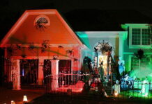 Halloween Holiday Spirit, and Outdoor Ideas Large house decorated for Halloween at night with bright orange and green spotlights, a spiderweb archway, and giant fake spiders crawling up the walls.