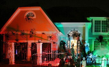 Halloween Holiday Spirit, and Outdoor Ideas Large house decorated for Halloween at night with bright orange and green spotlights, a spiderweb archway, and giant fake spiders crawling up the walls.
