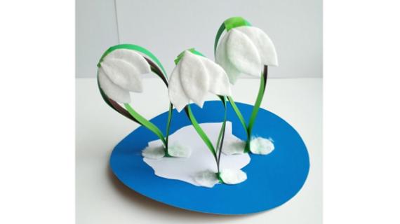 A handmade card features two white cotton pad swans on a pond with cattails, green leaves, and ripples. A yellow sun with rays appears in the blue sky.