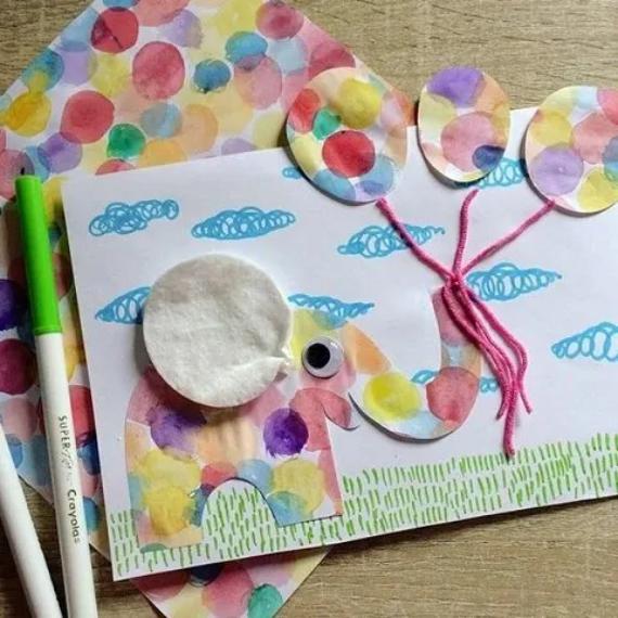 Funny Elephant cotton pad card featuring a polka dot elephant with a cotton ear and googly eye holding balloons with pink yarn, set against a cloudy sky.