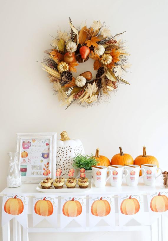 A festive table adorned with a wreath, colorful cupcakes, and decorative pumpkins for a seasonal celebration.