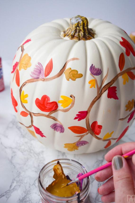 A person paints a pumpkin surrounded by colorful fall leaves, showcasing autumn creativity and seasonal decor.