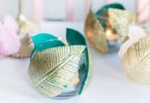 Creative Upcycling Ideas: Inspiration and craft ideas Glass candle holders adorned with metallic gold and teal textured leaves on a white surface, exuding a warm, elegant, and artistic ambiance.