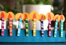45 Fun Clothespin Craft Ideas for Kids or Adults Colorful paper menorah with nine vibrant, striped candles on a blueWooden Clothespin base. Each candle has a yellow flame, creating a festive and joyful atmosphere.