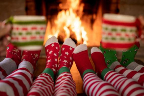 Fun Christmas Party feathering Five people wearing festive socks in front of a fireplace, holding mugs.