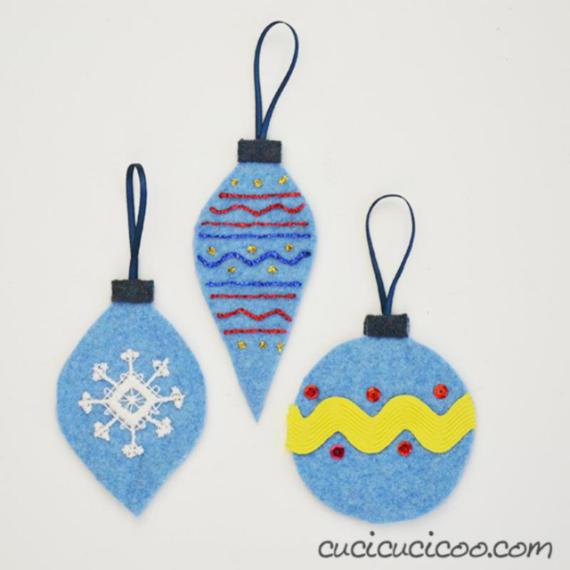 Three blue felt ornaments with various designs: a snowflake, zigzag lines, and colorful embroidery, each with a loop for hanging.