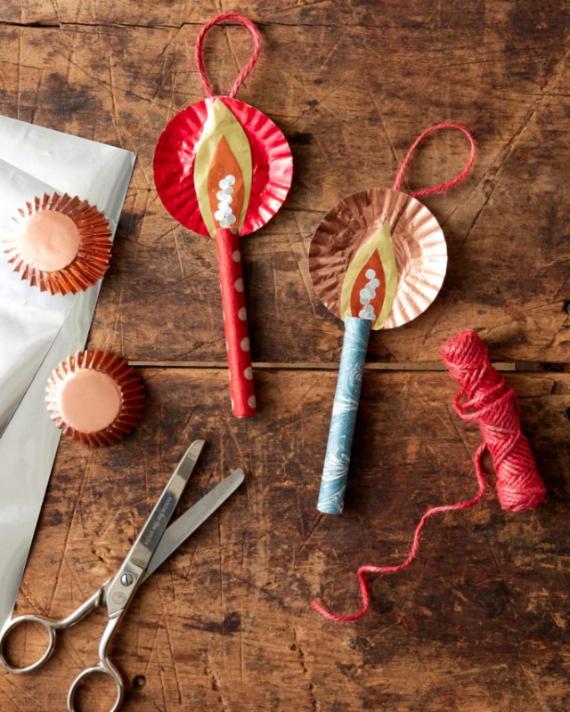 Crafts display: two colorful candle decorations made from paper plates and straws, alongside cupcake liners, scissors, and red string on a wooden table.