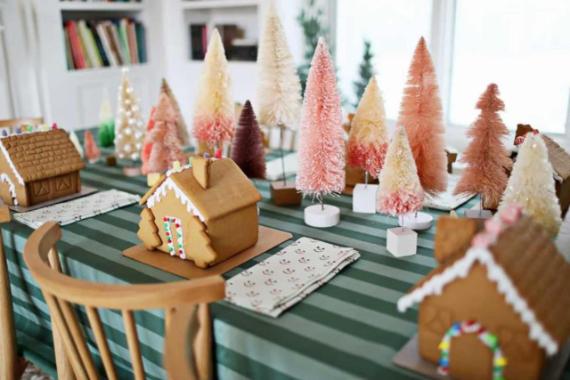 A festive table set with gingerbread houses and colorful, bottle-brush trees, surrounded by a green striped tablecloth.