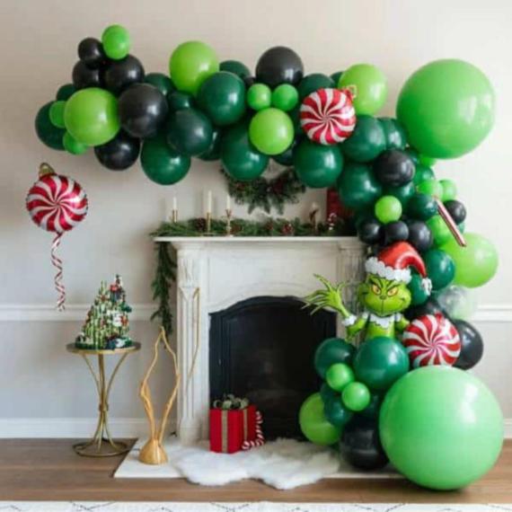 Festive CHRISTMAS PARTY IDEAS FOR KIDS feathering a fireplace with green and black balloon arch, featuring a mischievous character in a Santa hat. Decor includes candy-themed ornaments and a gift box.