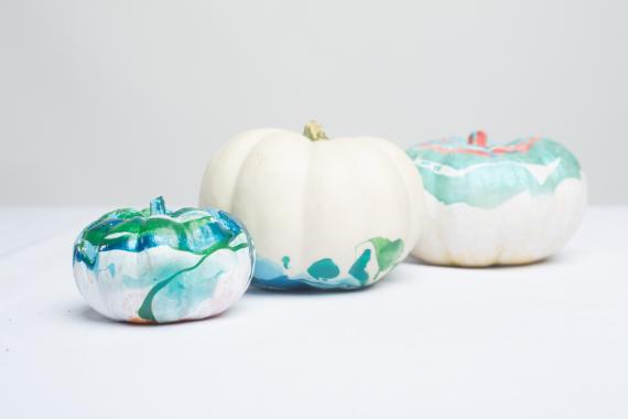 Bright fall decor ideas on 3 small white pumpkins on a white surface, partially painted with blue and green watercolor-like patterns, creating a calm and creative vibe.