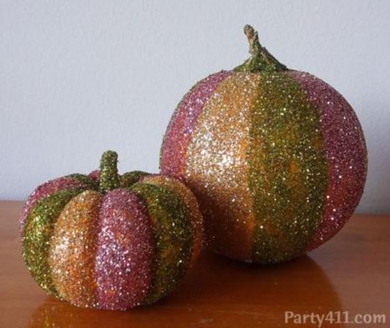 Two glittery Pink fall decor ideas of pumpkins sit on a wooden surface. They are covered in sparkling stripes of pink, green, and gold, creating a festive, playful atmosphere.