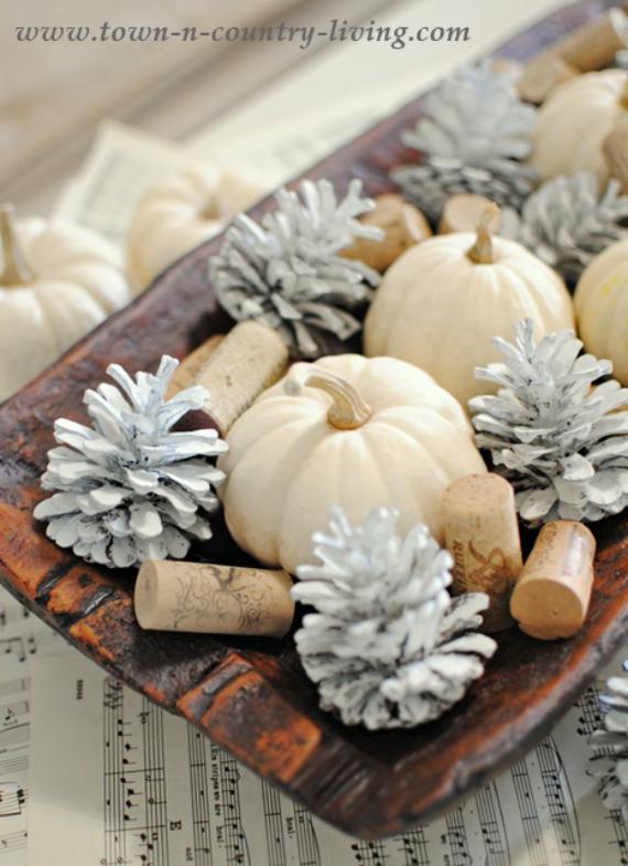 A rustic wooden tray filled with white mini pumpkins, silver-painted pinecones, and corks sits atop vintage sheet music, creating an unexpected fall color schemes for autumnal centerpiece.