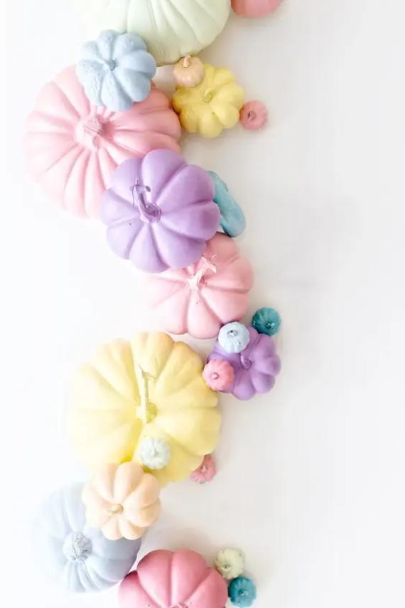 A collection of Pastel pumpkins decor in pink, purple, yellow, and blue arranged in a playful swirl on a white background, creating a whimsical, soft tone.