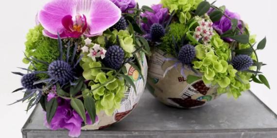 Non-traditional fall color palette of vibrant floral arrangements in rounded containers sit on a gray surface. Includes pink orchid, green hydrangeas, and purple thistles, exuding freshness.