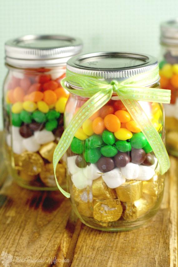 Mason jars filled with colorful layered candies, topped with a green ribbon. Gold-wrapped chocolates, marshmallows, and rainbow candy are visible, conveying an unexpected fall color schemes .