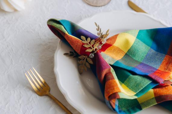 Fall decor with unexpected colors feathering white plate on a textured table with a colorful, checkered napkin. Gold cutlery, including a fork and knife, sits beside it. Elegant and festive.
