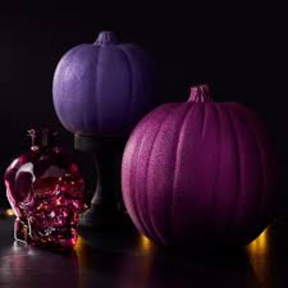 Two pumpkins in shades of purple sit beside a translucent red skull on a dark surface. Pink fall decor ideas with soft, glowing lights create a spooky, mysterious atmosphere.