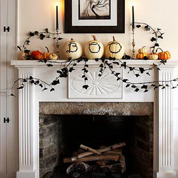 A white fireplace mantel decorated with pumpkins spelling "BOO," black candles, and autumn leaves. The scene is warm and festive with a Halloween theme.