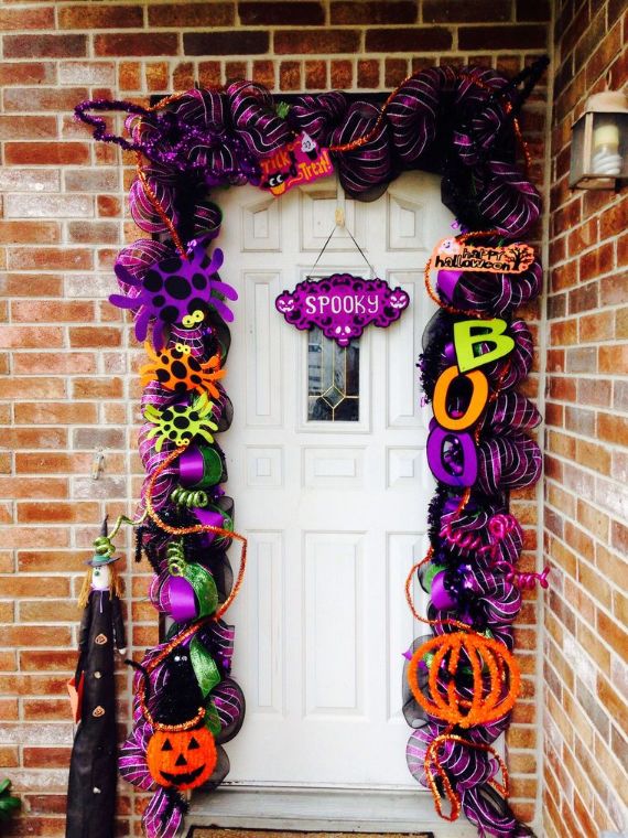 Front door adorned with vibrant Halloween decorations on a brick wall. Includes purple and orange garlands, "BOO," and "SPOOKY" signs for a festive feel.