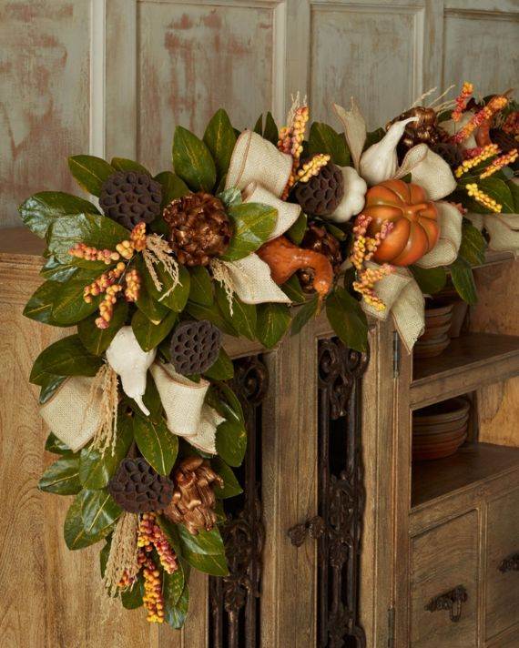 Natural autumn garland with leaves, pinecones, gourds, and berries draped over a rustic wooden cabinet, creating a cozy, seasonal ambiance.