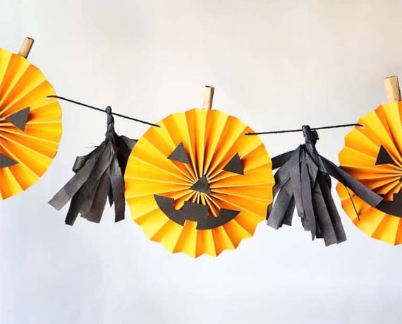 A festive garland features orange paper fan pumpkins with black jack-o'-lantern faces alternating with black paper tassels, creating a playful Halloween vibe.