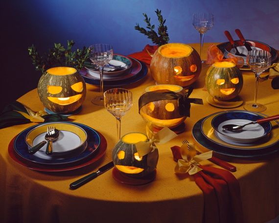 A festive table with carved pumpkins displaying playful faces, glowing warmly. Elegant place settings and colorful napkins enhance the cheerful atmosphere.