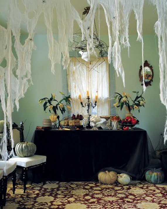 Elegant Halloween-themed dining room with cobwebs hanging from the ceiling, a black tablecloth, pale pumpkins, and a lit candelabra creating a spooky atmosphere.