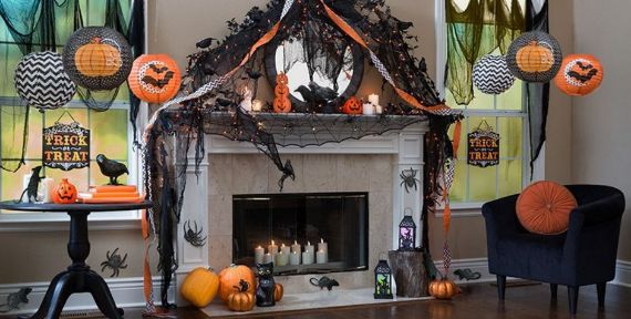 Halloween-themed living room with a decorated fireplace. Features spider webs, pumpkins, and paper lanterns. Warm, spooky ambiance with lit candles.