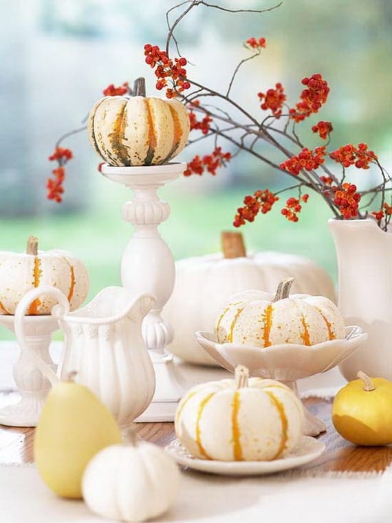 Festive autumn table setting with white pumpkins, decorative gourds, and orange berries in a vase. Bright and inviting with an autumnal theme.