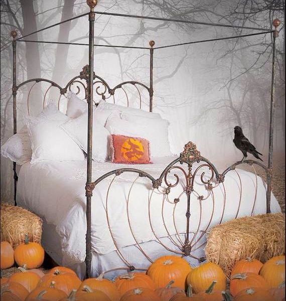 Vintage four-poster bed with white linens and pumpkin pillow, surrounded by pumpkins and hay bales. A crow perches on the iron frame, set against a foggy forest background.