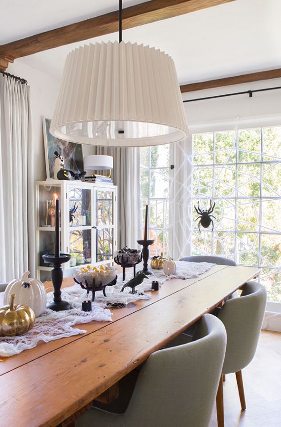 Dining room with a rustic wooden table, Halloween decor including pumpkins and spider decorations. A large, pleated white lamp hangs above.