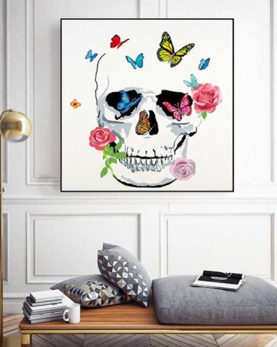 A vibrant painting of a skull adorned with colorful butterflies and roses hangs in a minimalist living room, evoking a lively and whimsical atmosphere.