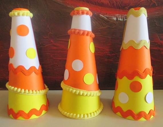 Three colorful cone-shaped decorations with dots and zigzag patterns in orange, yellow, and white against a red and brown backdrop. Playful and festive.