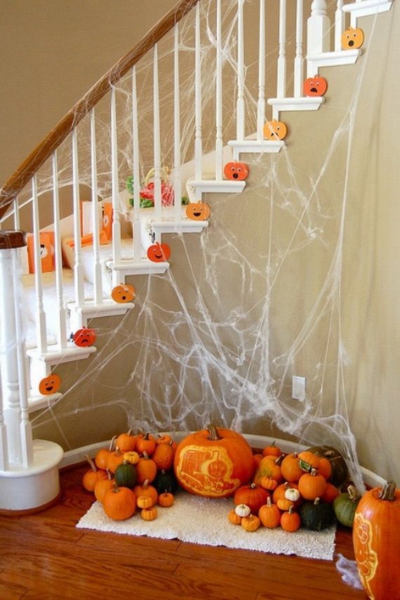 A staircase decorated for Halloween with white cobwebs, orange paper pumpkins on steps, and a cluster of real pumpkins, some carved, at the bottom.