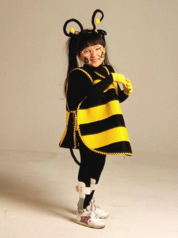 A child in a cheerful bee costume with black and yellow stripes, wearing glasses and smiling. They have bee antennae on their head and yellow gloves.
