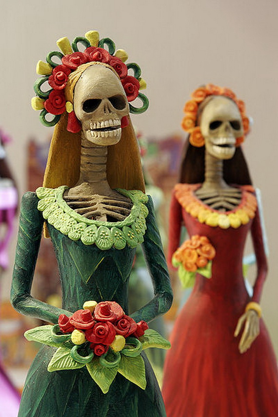 Colorful ceramic skeletal figures in elegant dresses, adorned with floral headpieces, embodying festive and cultural elements of Día de los Muertos.
