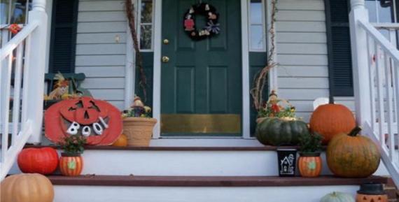 Festive porch with pumpkins, a "Boo" sign, and Halloween decor. Green door adorned with a wreath, creating a welcoming, autumnal atmosphere.