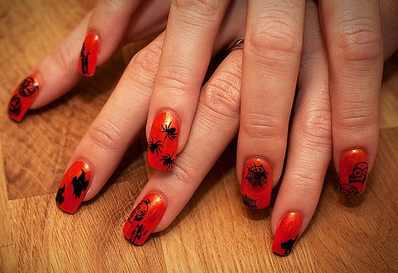 Red nails with black Halloween designs, like spiders, webs, and bats, on a wooden surface. The festive style conveys a spooky, playful vibe.